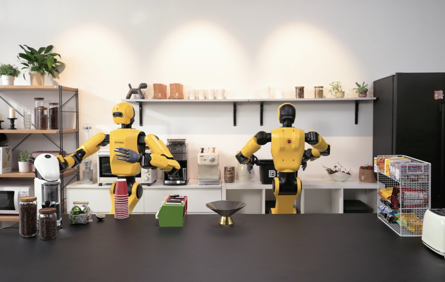 그림 9.2: World Robot Conference 공식 DexForce 응용 사례의 실물 W1 Pro 휴머노이드 두 대. 카페 형태 작업대와 다양한 물체 앞의 물리 배치는 보여 주지만 자율 커피 제조, 작업 성공률 또는 시뮬레이션 타당성을 입증하지 않는다. 출처: World Robot Conference DexForce 공식 출품사 사례 페이지, 학술 리뷰 목적의 공정 이용